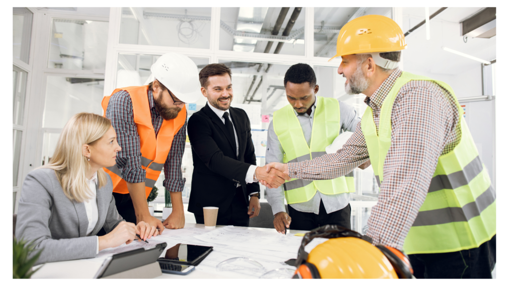 Collaborative Construction Site Meeting and Handshake A diverse team of architects and engineers in high-visibility vests and hard hats gather around a white table covered in blueprints. A man in a suit shakes hands with a site manager in a yellow vest while others look on in a modern, bright office.