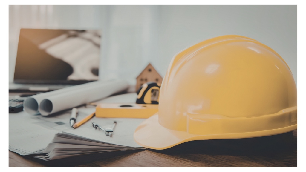 Construction Engineering and Architectural Workspace A close-up shot of a yellow hard hat sitting on a wooden desk alongside architectural blueprints, a laptop showing floor plans, a level, a tape measure, and various drafting tools.